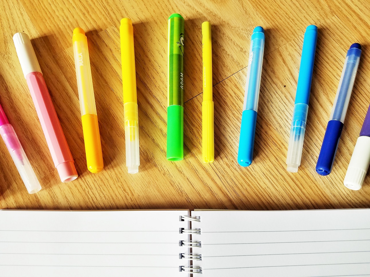 Spelling Test - colourful rainbow pens arranged around a school notebook